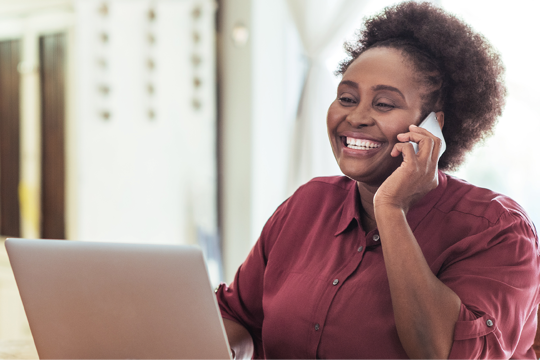 A woman on the phone smiling whilst looking at her laptop A woman on the phone smiling whilst looking at her laptop